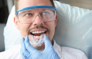 Dentist trying on mouthguard on man patient's teeth.